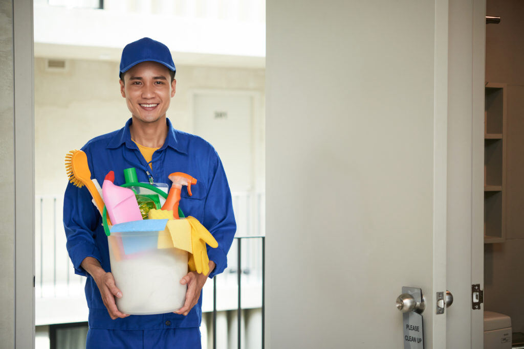 cheerful-asian-male-janitor-walking-into-hotel-room-carrying-supplies-bucket-1024x683