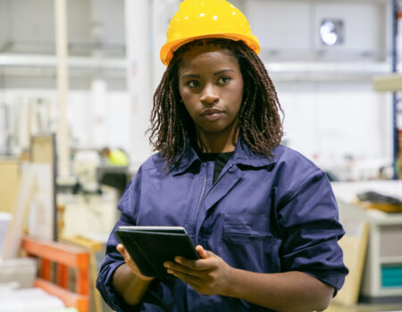 Content female plant worker standing with tablet and looking away. Portrait of pensive African American woman doing her job, thinking and wearing uniform. Manufacture and digital technology concept